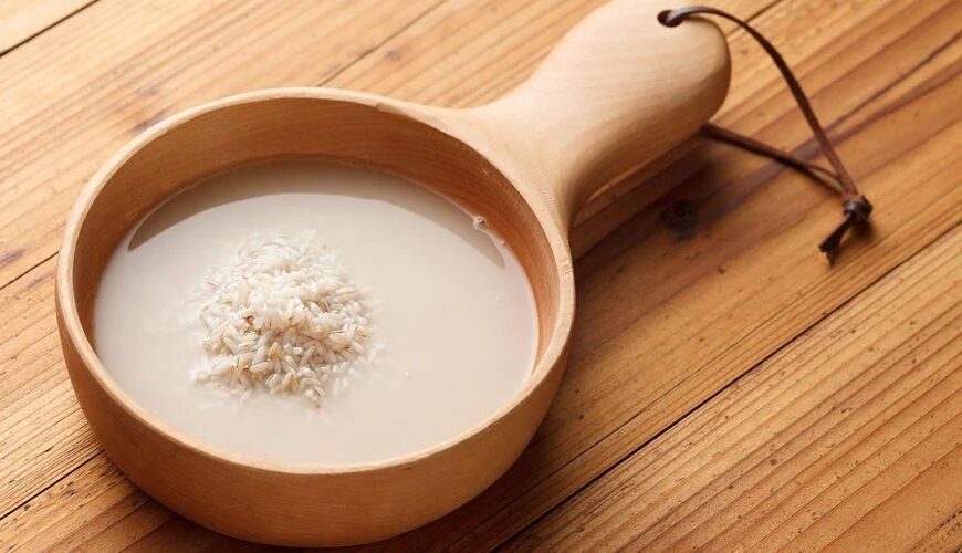 a wooden spoon with a bowl of rice and water